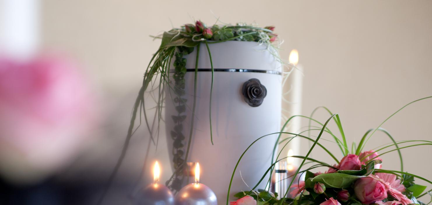 Blumenschmuck mit rosa Rosen und grünen Pflanzenarrangements auf einem Tisch, umgeben von Kerzen und einem weißen Behälter.