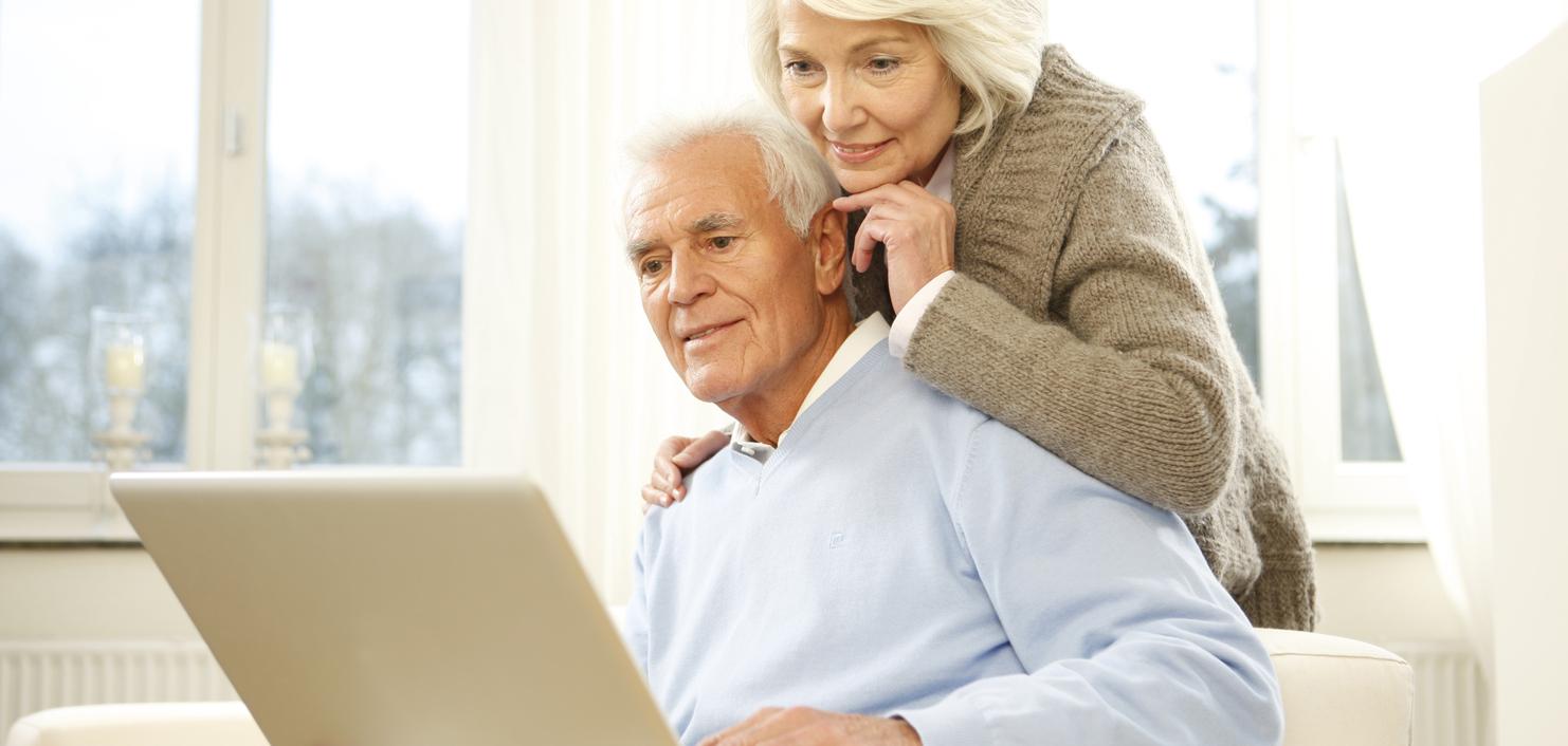 Paar sitzt auf einer Couch und schaut gemeinsam auf einen Laptop in einem hellen Raum.